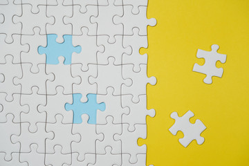 Fragment of a folded white jigsaw puzzle and a pile of uncombed puzzle elements against the background of a yellow surface.