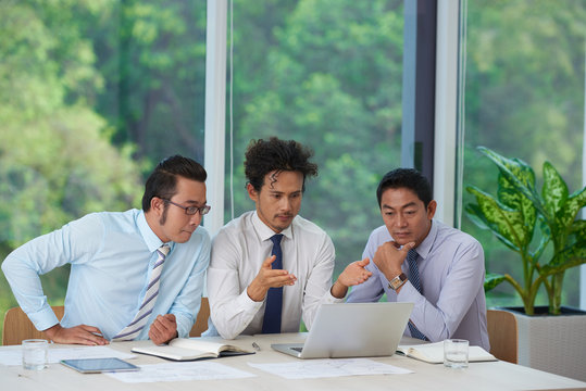 Group of serious Vietnamese financial managers reading e-mail with important data on laptop screen