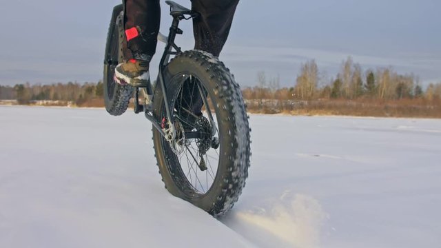 Professional extreme sportsman biker riding fat bike in outdoors. Cyclist ride in winter snow forest. Man does trial trick wheelie on mountain bicycle with big tire in helmet and glasses.