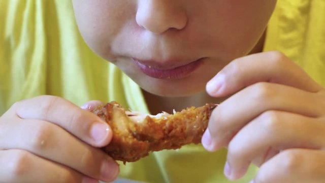 Closeup view of hungry cute little white kid eating tasty barbecued chicken wings with great appetite at fast food restaurant. Real time full hd video footage.