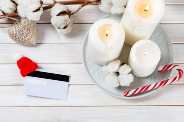 Fototapeta na wymiar Christmas online shopping. Credit card with christmas hat on white wooden background with candles and cotton branch. top view. Discount card Mock up. Winter holidays sales. Copy space