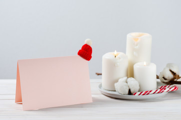 Letter to Santa with copy space on white wooden background. Mock up. Blank greeting card with christmas hat, candles, candy cane and cotton branch. Side view