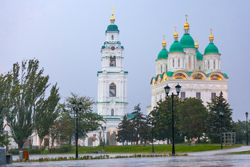 Fototapeta na wymiar Assumption Cathedral of the Blessed Virgin Mary, white christian church, in heavy rain opposite the lamppost on the park's footpath. Historical and architectural complex Astrakhan Kremlin, Russia.