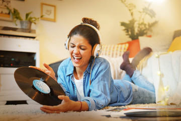 Vibrant young brunette listening to vinyl records on floor at home
