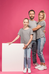 Fototapeta premium beautiful family posing with empty placard, isolated on pink