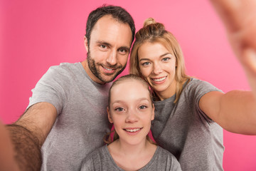 smiling family taking selfie together, isolated on pink