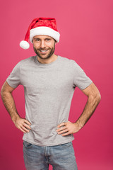 Fototapeta premium portrait of handsome smiling man in santa hat at christmastime, isolated on pink