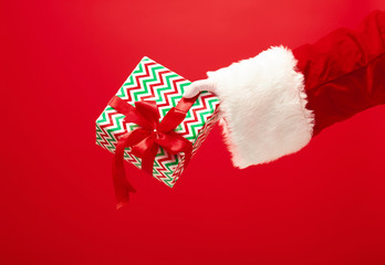 The hand of santa claus holding a gift on red background. The season, winter, holiday, celebration, gift concept