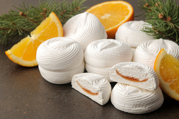 Sweet white marshmallows with orange filling and fresh oranges and a sprig of Christmas trees on a dark background Sweets. dessert.