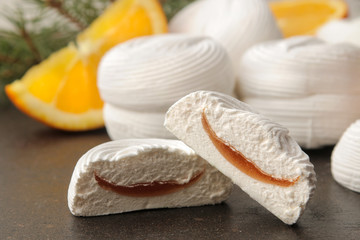 Sweet white marshmallows with orange filling and fresh oranges and a sprig of Christmas trees on a dark background Sweets. dessert.