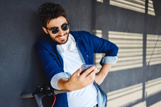 Portrait of smiling young man with electric scooter looking at cell phone