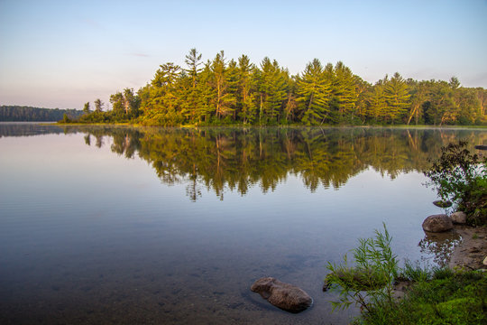 Wilderness Island. Pine forest island bathed in golden sunlight with forest reflected in the calm lake water of the Hiawatha National Forest in Michigan.
