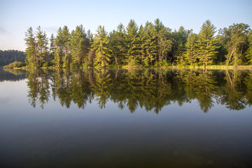 Fototapeta na wymiar Morning Forest Reflections. Gorgeous wilderness forest reflected in the pristine lake waters of northern Michigan in the Hiawatha National Forest 