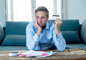 Upset man in stress paying credit card debts and counting finance with calculator and bank papers