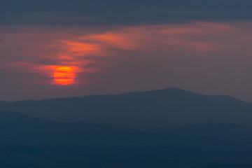 Mystic sunset in the Tuscany region with red solar disk and silhouettes of the hills, Italy