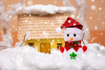Toy snowman in  snow near the house during snowfall_
