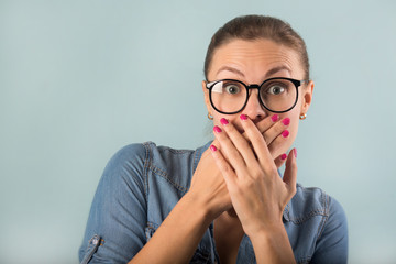 beautiful young girl in a denim shirt and glasses on a blue background with astonishment on her face