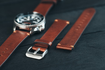 Mens diver watch with brown leather handmade watch strap on black wooden surface. Closeup. Copy...