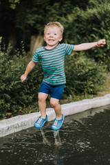 little boy jumping in a puddle in summer