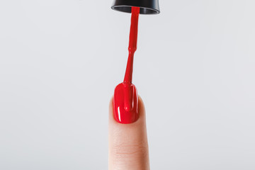 cropped view of woman applying red nail polish on fingernail isolated on grey