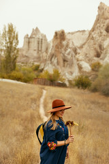Beautiful Woman In Hat With Flowers At Field With Rocks Valley