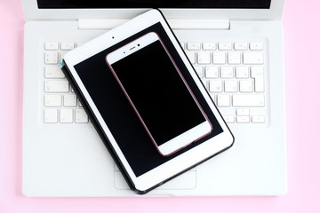Tablet and mobile phone with black screens on white laptop keyboard. Electronic touch device with selective focus on pink background. Mobility web office with touchscreen