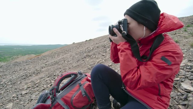 Young Asian female hiker taking photos of landscape with professional camera from mountain top