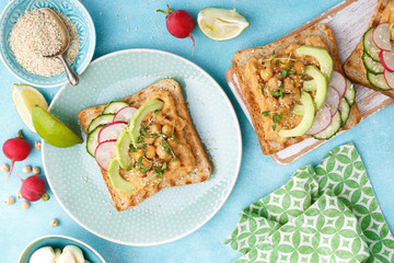 Toasts with chickpea hummus, avocado, fresh radish, cucumber, sesame seeds and flaxseed sprouts. Diet breakfast. Delicious and healthy plant-based vegetarian, vegan food. Flat lay. Top view