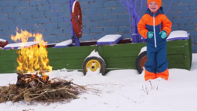 Happy village children play around campfire from branches against background of toy pirate ship. Children are happy together on winter vacation. Snow Christmas Eve
