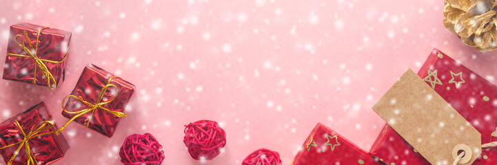 Panoramic Christmas background with snow and red and golden gift or present box, pine cone and holiday decorations on pink pastel table top view. Greeting card. Flat lay. ..