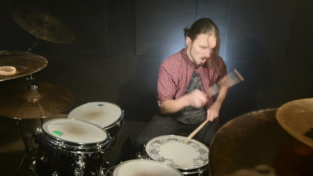 The long-haired drummer finishes playing the drum set in a dark room on a black background. Rock musician. Static plan. Wide angle