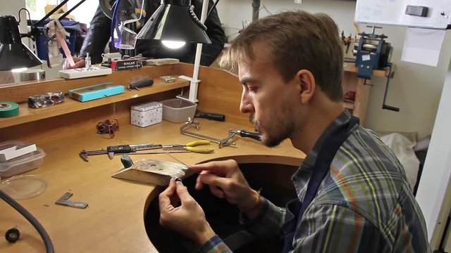 man jeweler processes the surface of the billets for silver ring with a file(tool), workshop jewelry