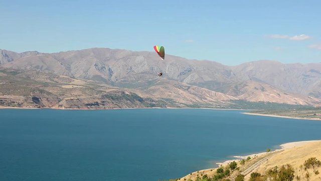 couple of people on a paraglider flies over the reservoir Charvak, mountains in the background, Chatkal Mountain, Uzbekistan