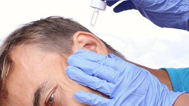doctor in blue medical gloves with a pipette, drops a medicament in the ear of patient and massages the ear, closeup, white background
