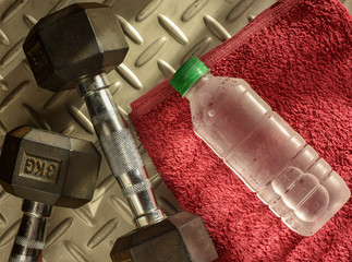 Bottle of fresh cold water on red towel with dumbbells and checker plate background, afternoon...