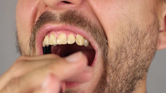 man with beard and mustache opens his mouth and thoroughly brushes his molar teeth with black toothbrush without toothpaste, front view, closeup