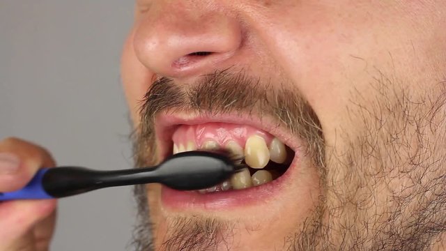 side view of man mouth with beard and mustache thoroughly brushes his teeth with black toothbrush without toothpaste, movements from side to side, gum massage, close-up