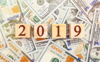 Wooden cubes with numbers 2019 on background of dollar bills. Top view.