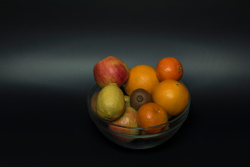 Orange mandarin kiwi apple with black background in vitreous bowl