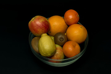 Orange mandarin kiwi apple with black background in vitreous bowl