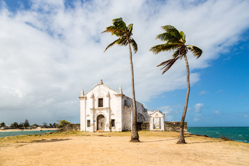 Church and fortress of San Antonio on Mozambique island, with two palm trees on sand. Indian ocean coast, Nampula province, Mozambique. Fortim de Santo António na Ilha de Moçambique.  - obrazy, fototapety, plakaty