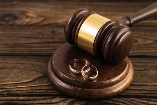a pair of gold engagement rings, a judge's hammer on a wooden table background. family law, divorce and conflict.
