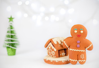 Gingerbread man near the house on the background of beautiful bokeh snowflakes. Christmas food decorations.
