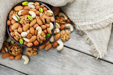 Wooden bowl with nuts on a wooden background, near a bag from burlap.