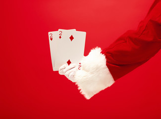 The hand of santa claus holding a playing cards on red background. The season, winter, holiday, celebration, gift concept