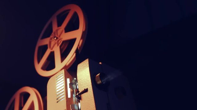 Vintage objects, cinematograph concept. Retro film projector playing in the dark room. Old-fashioned antique super 8mm film projector projecting beam of light. 4k.