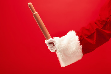 The hand of santa claus holding a culinary rolling pin on red background. The season, winter, holiday, celebration, gift concept