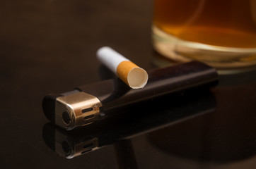 a glass of whiskey, cigarette and lighter on the black glass table