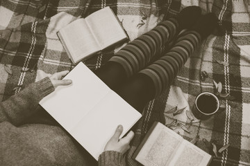 Women's hands and feet in sweater and cozy socks holding cup of hot coffee