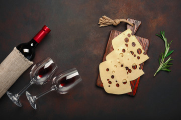 Bottle of wine, two glasses and maasdam cheese sliced on a cutting board on rusty background